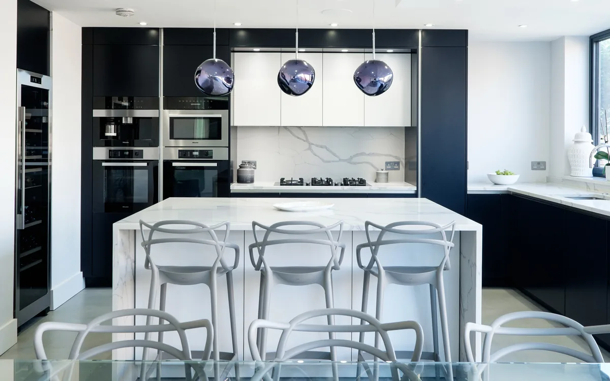 Navy and white kitchen with a marble waterfall island, bar stools and three smoky glass pendant lights